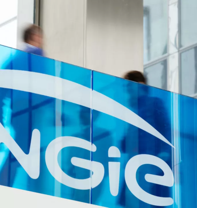 Blue-tinted glass with the Engie logo in white; blurred figures are visible through the glass in a modern building interior.