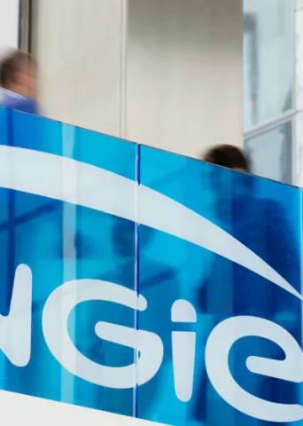 Blue-tinted glass with the Engie logo in white; blurred figures are visible through the glass in a modern building interior.