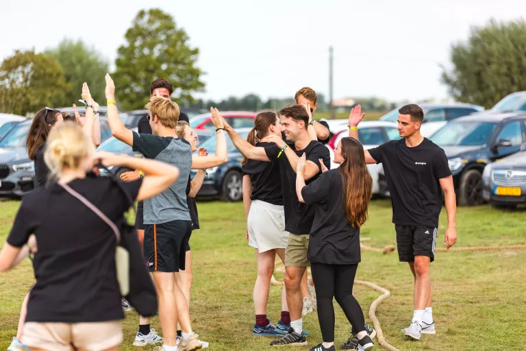 Group of Springbok Agency people outdoors celebrating with high-fives and smiles on a grassy field, surrounded by parked cars. The mood is energetic and joyful.