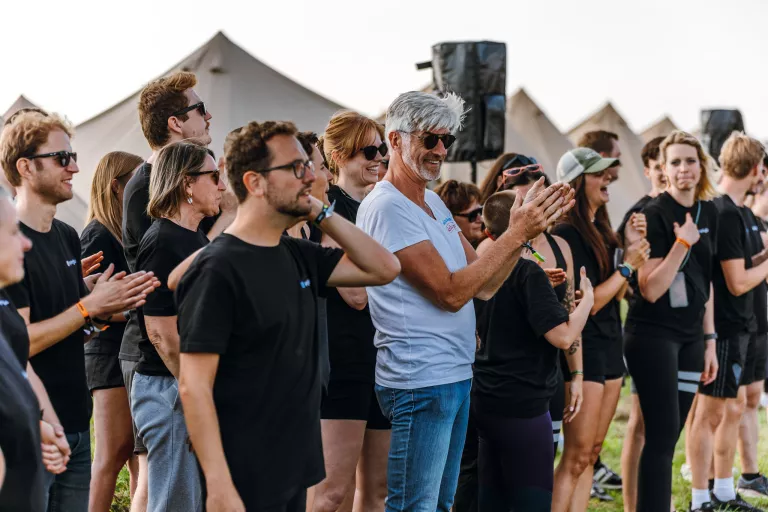 A group of people at Springbok's outdoor team event, all wearing Springbok black shirts and sunglasses, standing outdoors near tents, happily clapping and smiling.