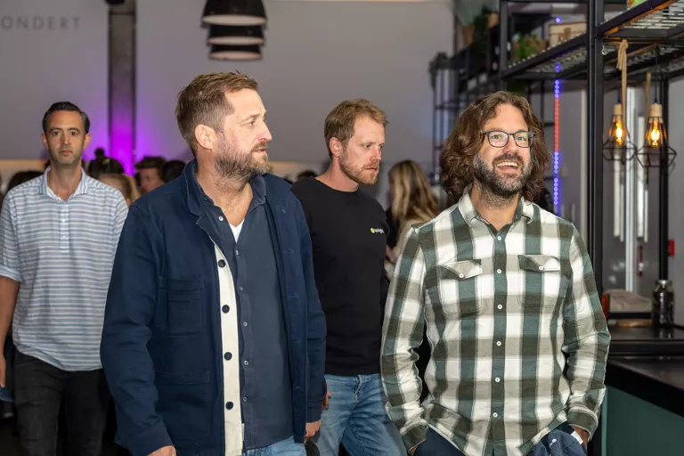 Four male Springbok team members casually walks through an indoor space. They look relaxed and engaged. Modern lighting and shelves create a warm atmosphere.